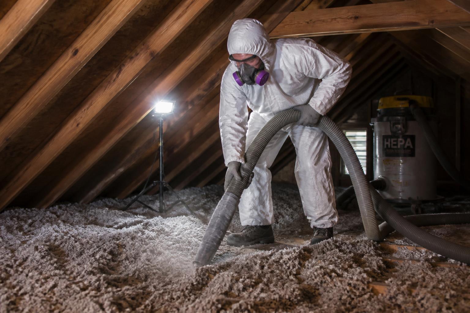 Technician in protective suit removing old contaminated attic insulation