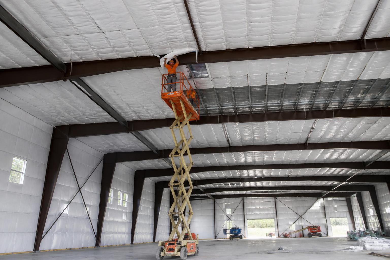 Crew on scissor lifts installing insulation in a large commercial building