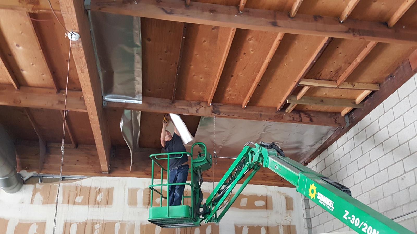 Installer on a boom lift stapling reflective radiant barrier to roof decking