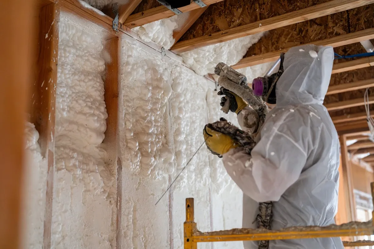 Technician in protective suit spraying closed-cell foam insulation onto wall framing